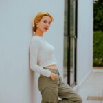 Fashionable woman in casual attire leaning against a modern white wall outdoors.